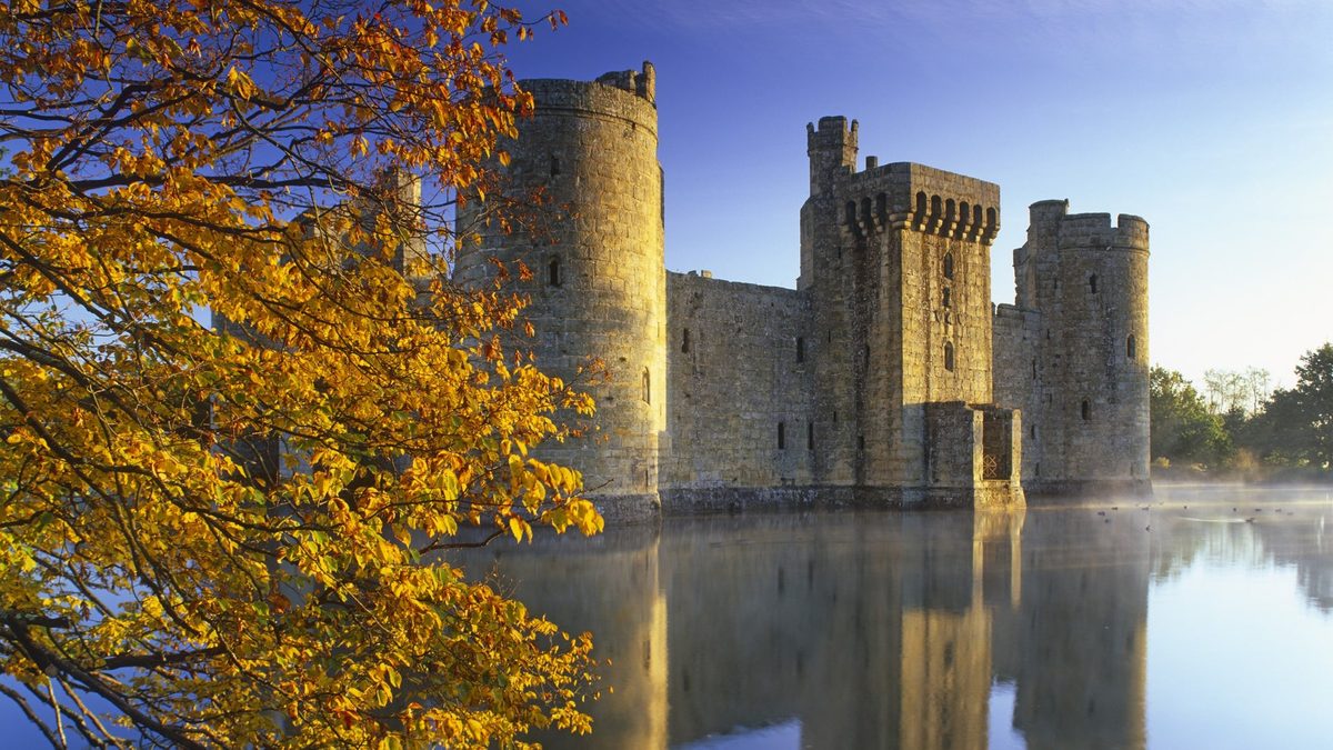Bodiam Castle's towers reflected in the moat, framed by autumn leaves, home of Spell Quest
